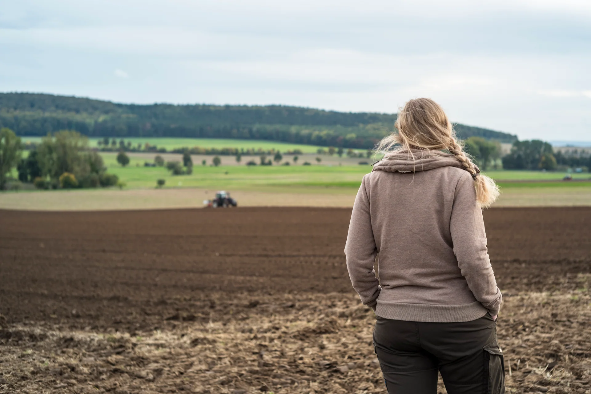 Kvinna ser ut över en plöjd åker med traktor i fjärran